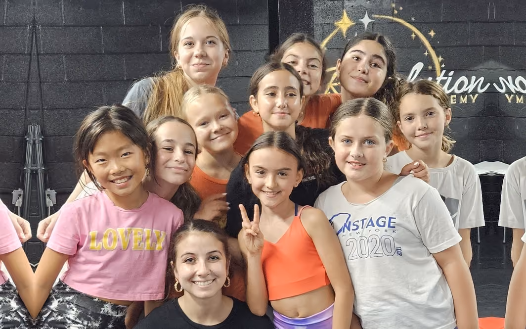 RDA dancers gathered with their instructor holding a First Day of Dance Classes sign in the studio