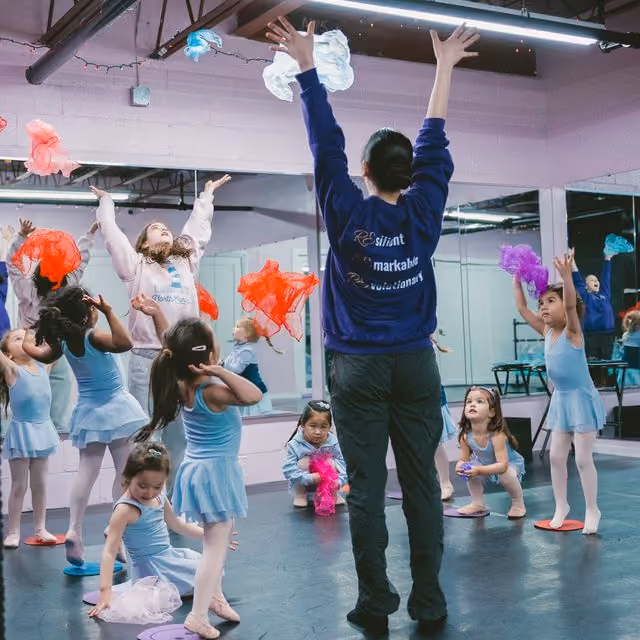 An RDA teacher and a class of preschool ballet dancers tossing colorful scarves in the air at the Tenafly studio