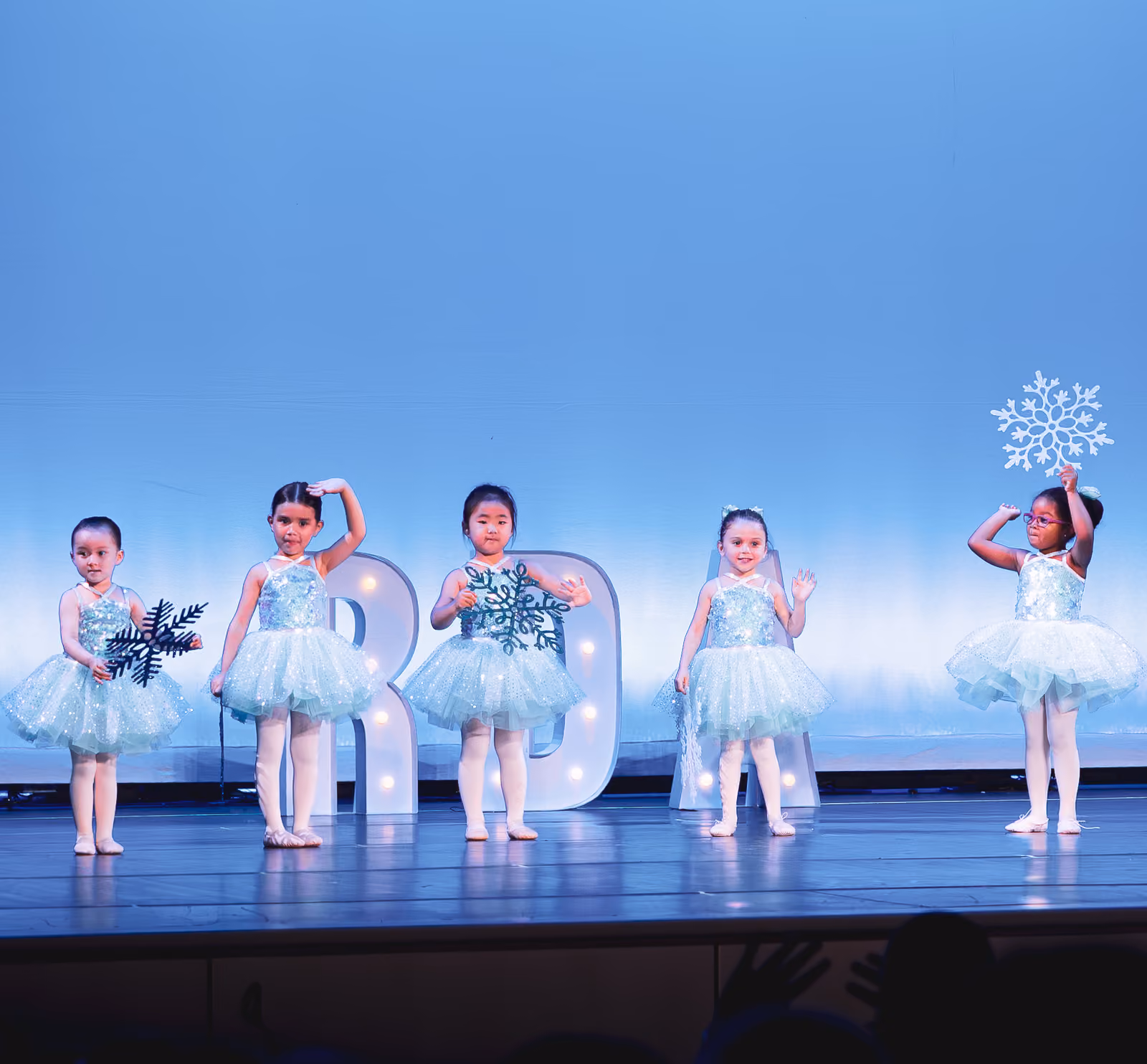 Five young RDA dancers in sparkly blue tutus holding snowflakes on stage at the Revolution Dance Academy recital