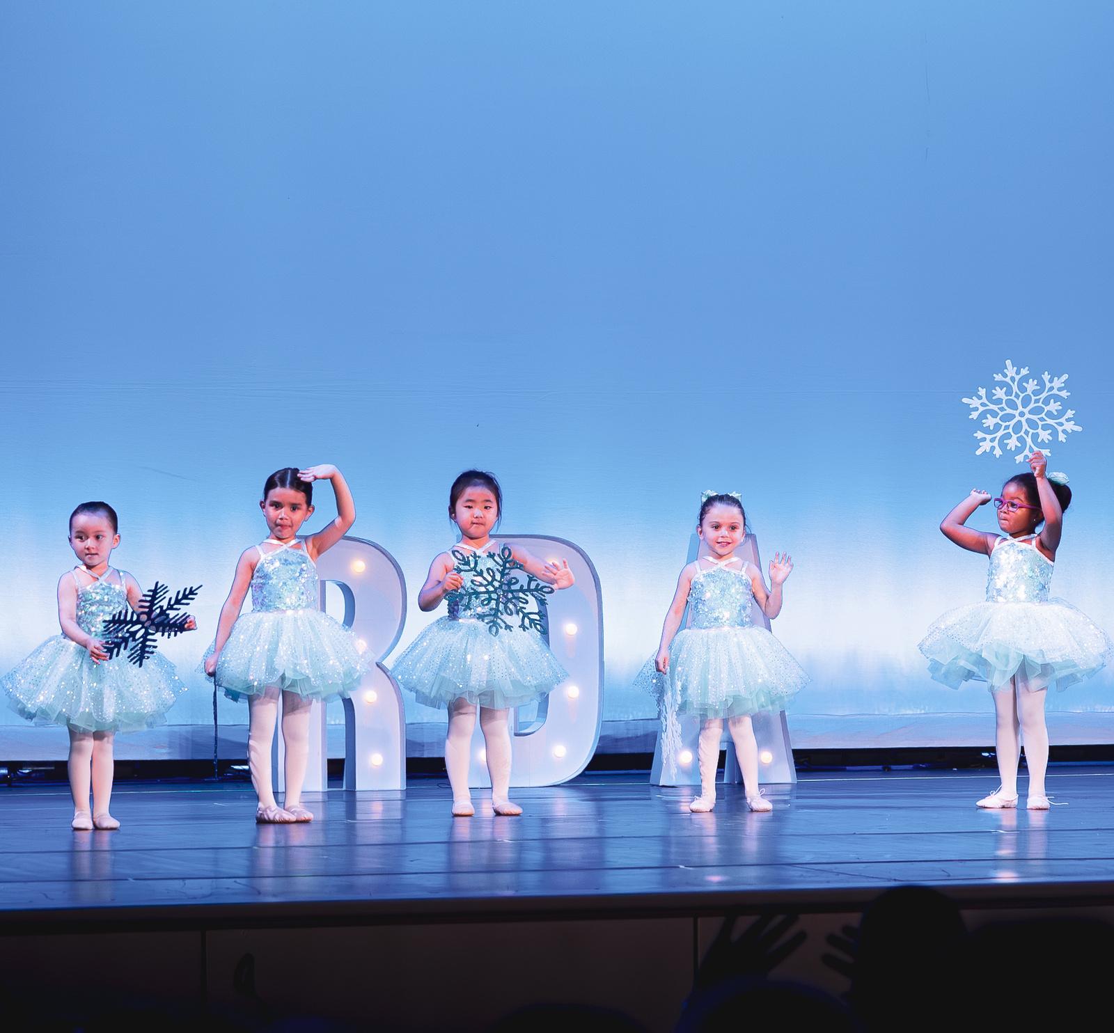 Five young RDA dancers in sparkly blue tutus holding snowflakes on stage at the Revolution Dance Academy recital