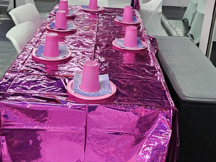 Pink foil-covered party table with cups and plates ready for guests at an RDA birthday party