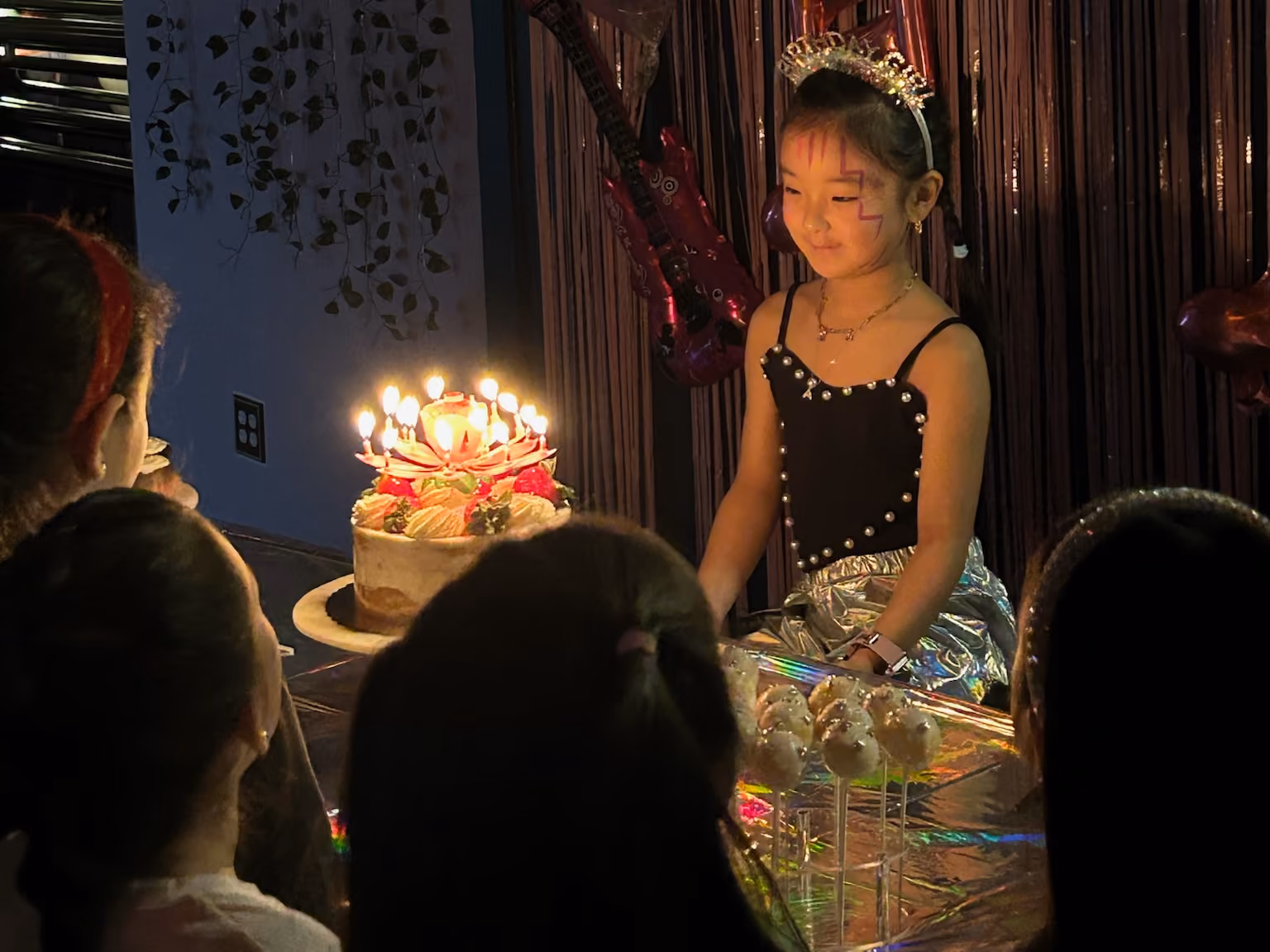 Birthday girl in a tiara blowing out candles on her cake at an RDA dance party