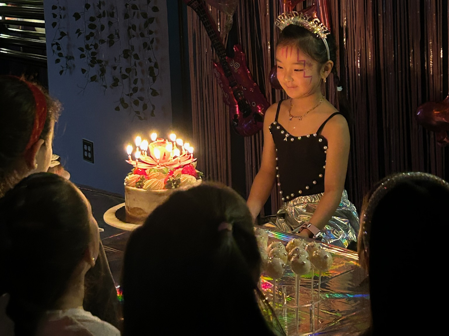 Birthday girl in a tiara blowing out candles on her cake at an RDA dance party