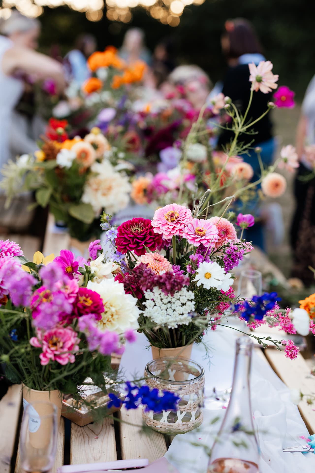 Jars of cut dahlias and cosmos down a long table at an evening gathering