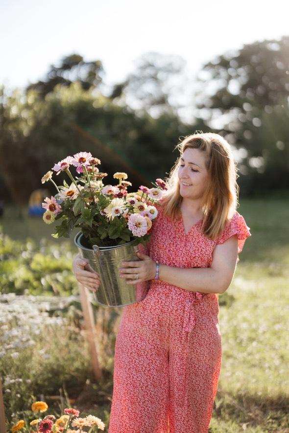 A woman carrying a bucket of freshly cut dahlias through the field