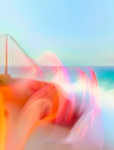 Blurred image with bright orange and pink light streaks near a coastal bridge under a clear blue sky.