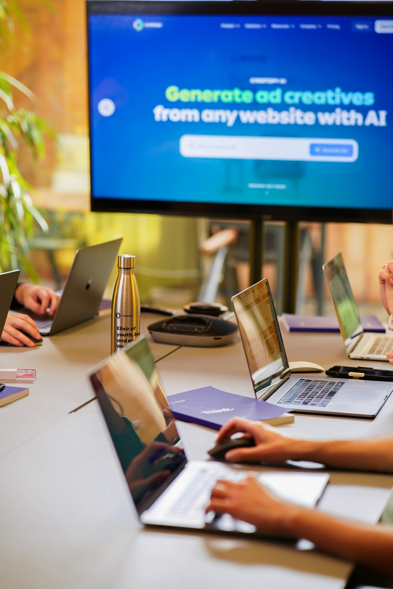 Laptops on a shared office table in front of a large screen