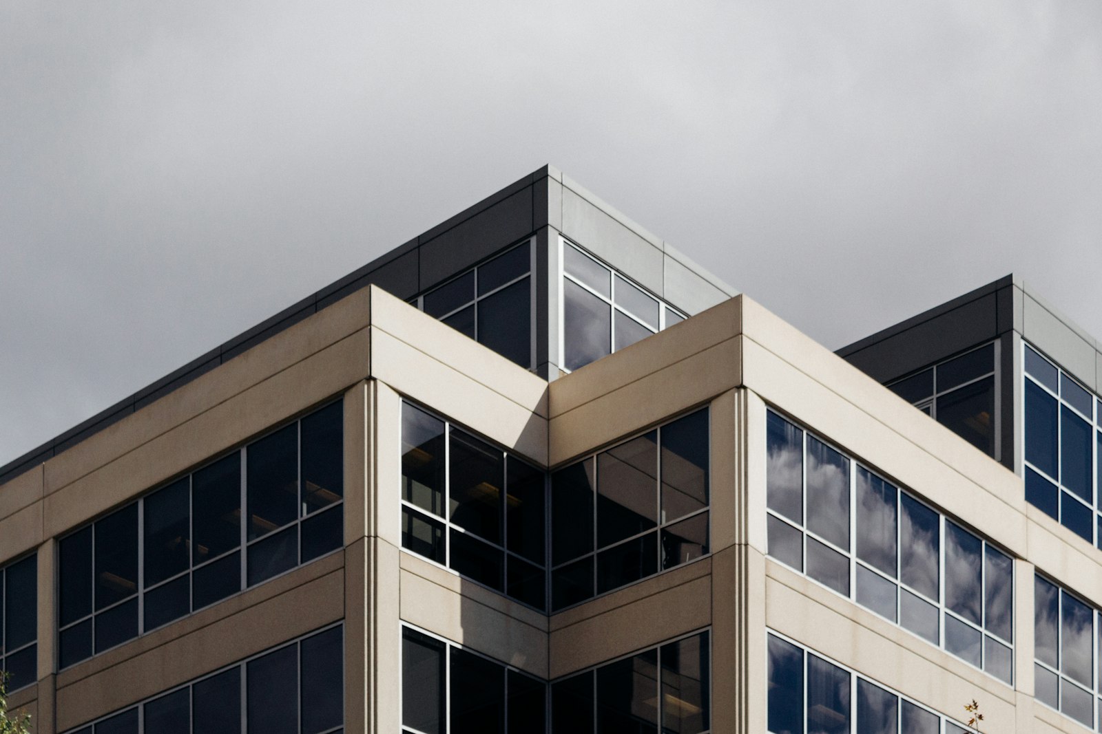 Corner of a modern office building with glass windows against a grey sky