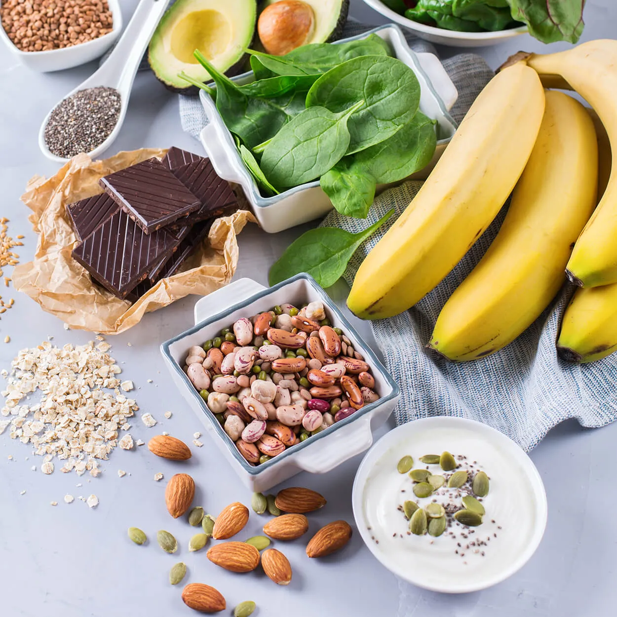 A flat lay of nutritious foods including bananas, spinach, beans, nuts and yogurt