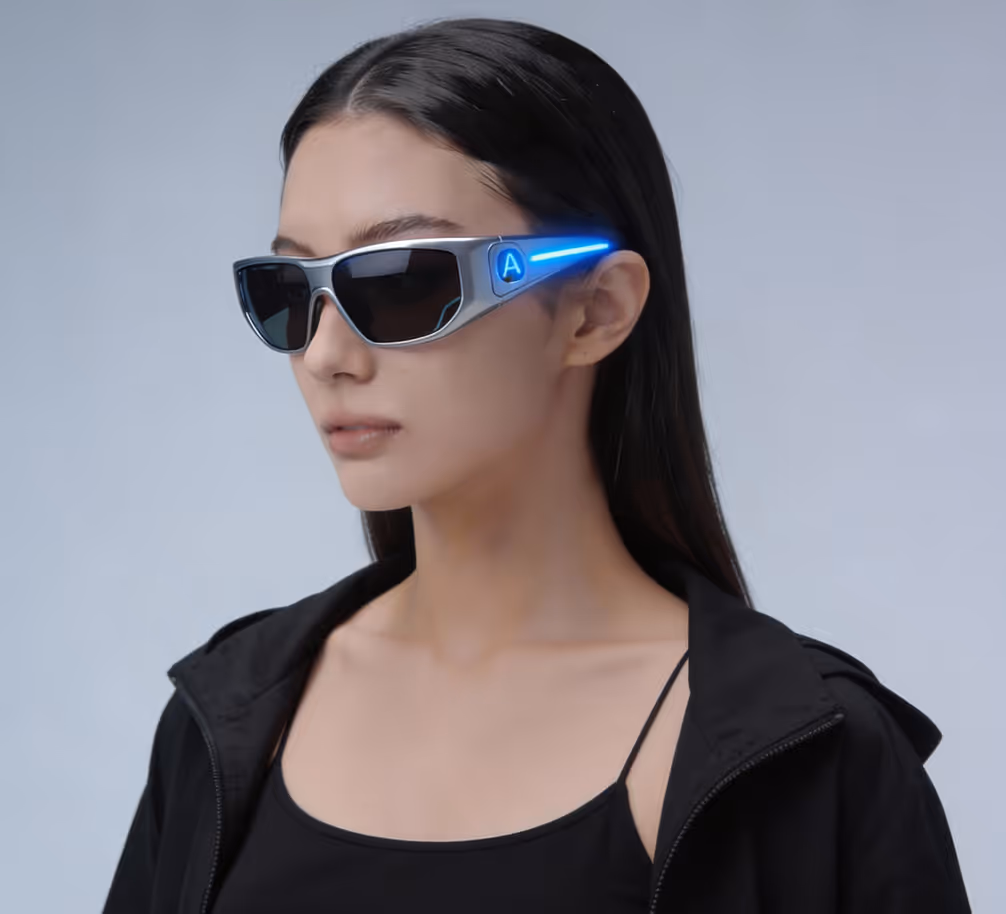 Woman with short black hair wearing futuristic silver sunglasses with glowing blue light on the sides and an illuminated letter A.