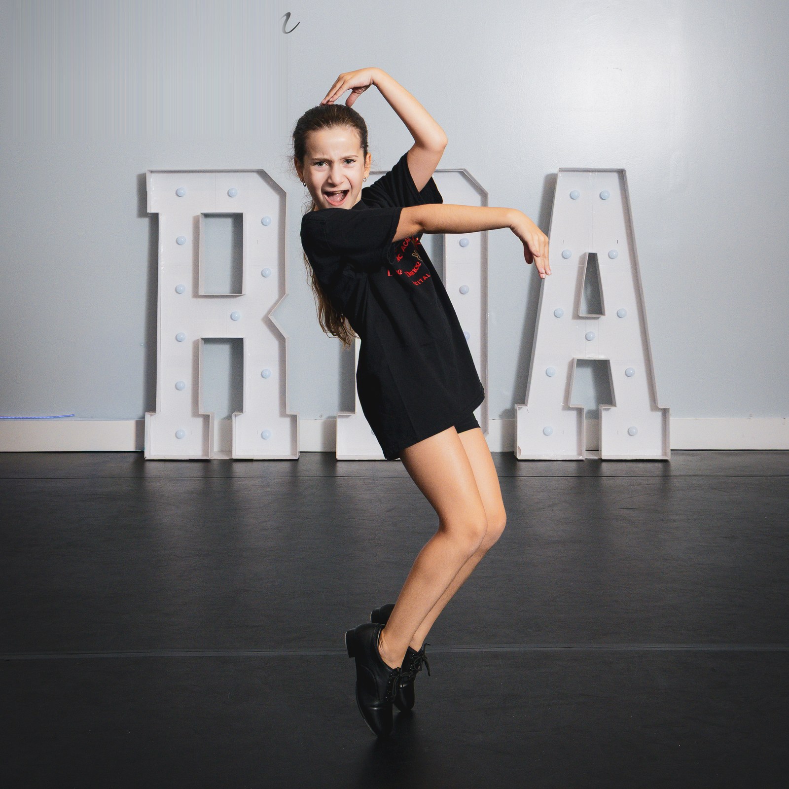 A young tap dancer posing on her toes in front of the RDA marquee letters