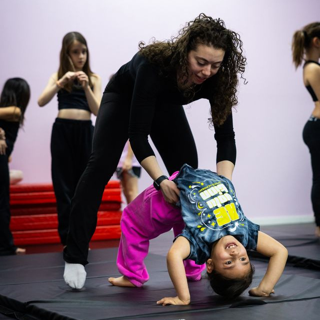 An RDA acro coach spotting a young student holding a bridge on the mats in the Tenafly studio