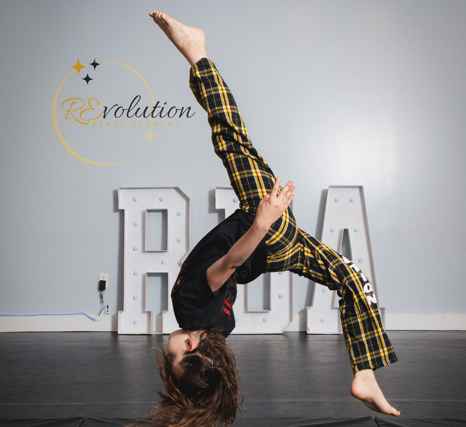 An RDA acro dancer mid-flip in front of the studio's RDA marquee letters