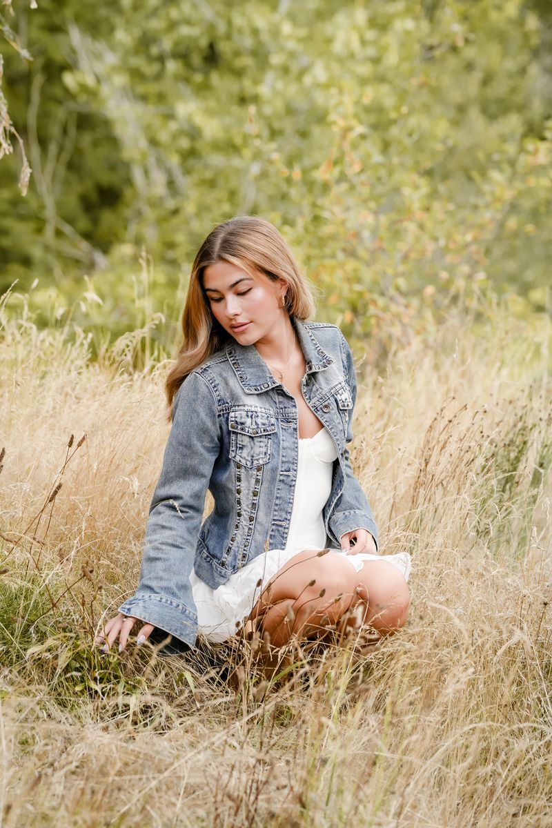 Senior in a denim jacket sitting in tall grass