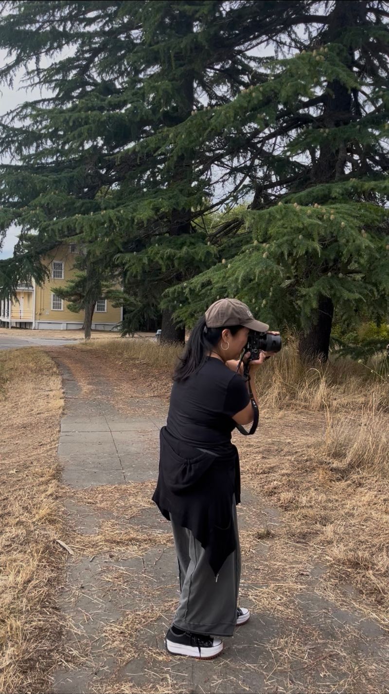 Kelly Goto standing outdoors with a camera raised to her eye