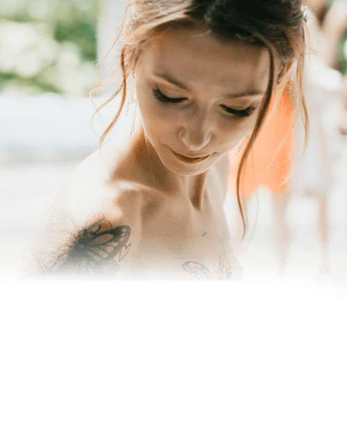 Softly faded portrait of a bride looking down, with a butterfly tattoo on her shoulder
