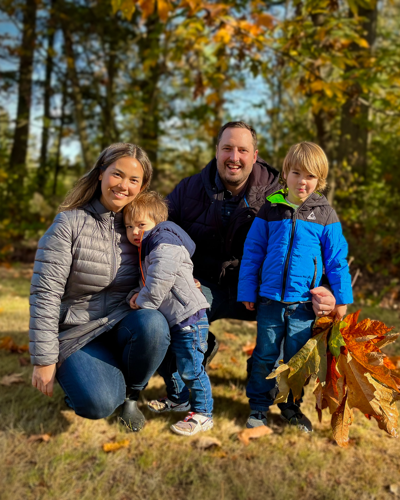 Vertical family portrait of parents and two children together outdoors among autumn leaves