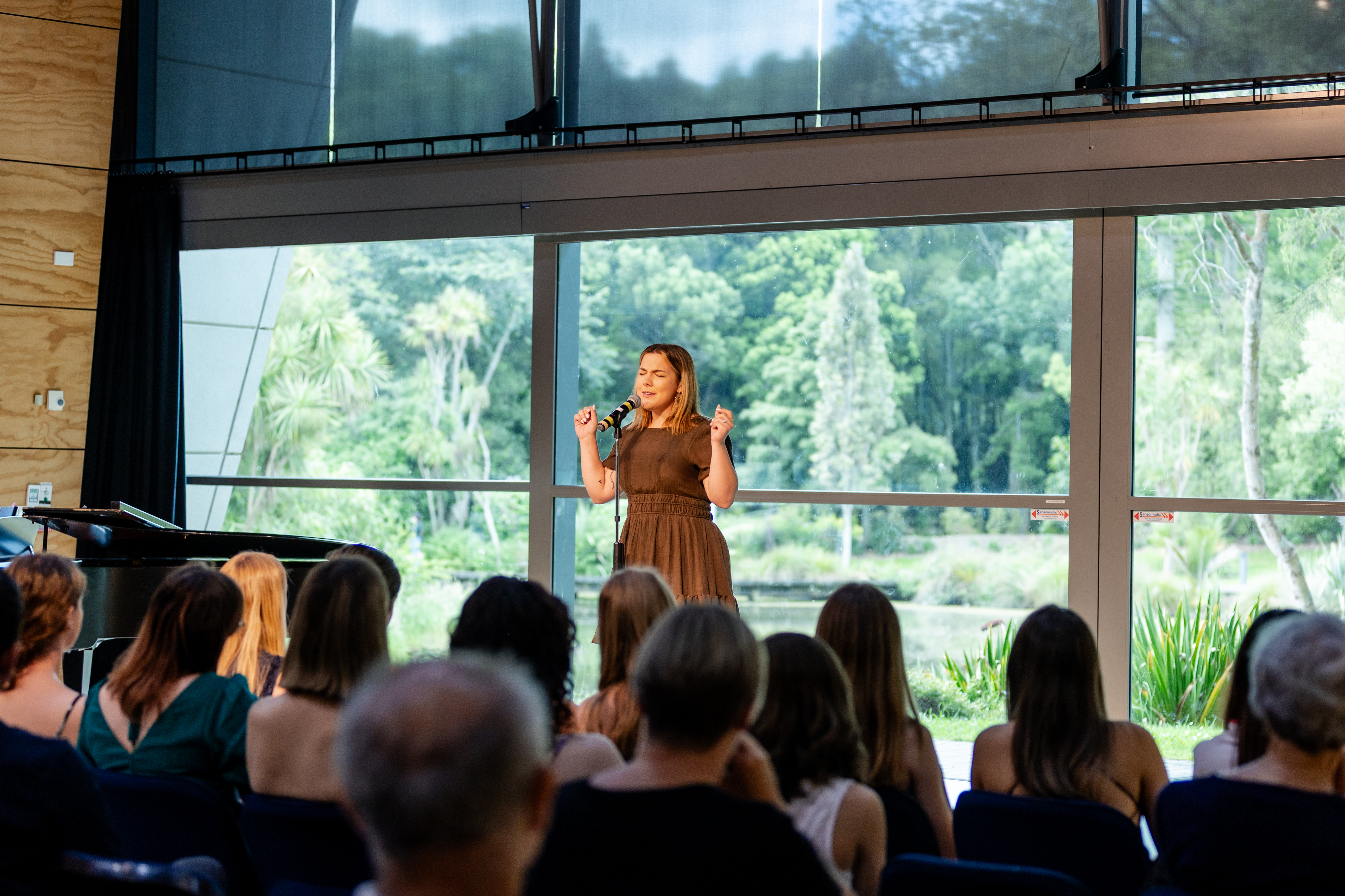 A singer performing at a vocal showcase in front of large windows