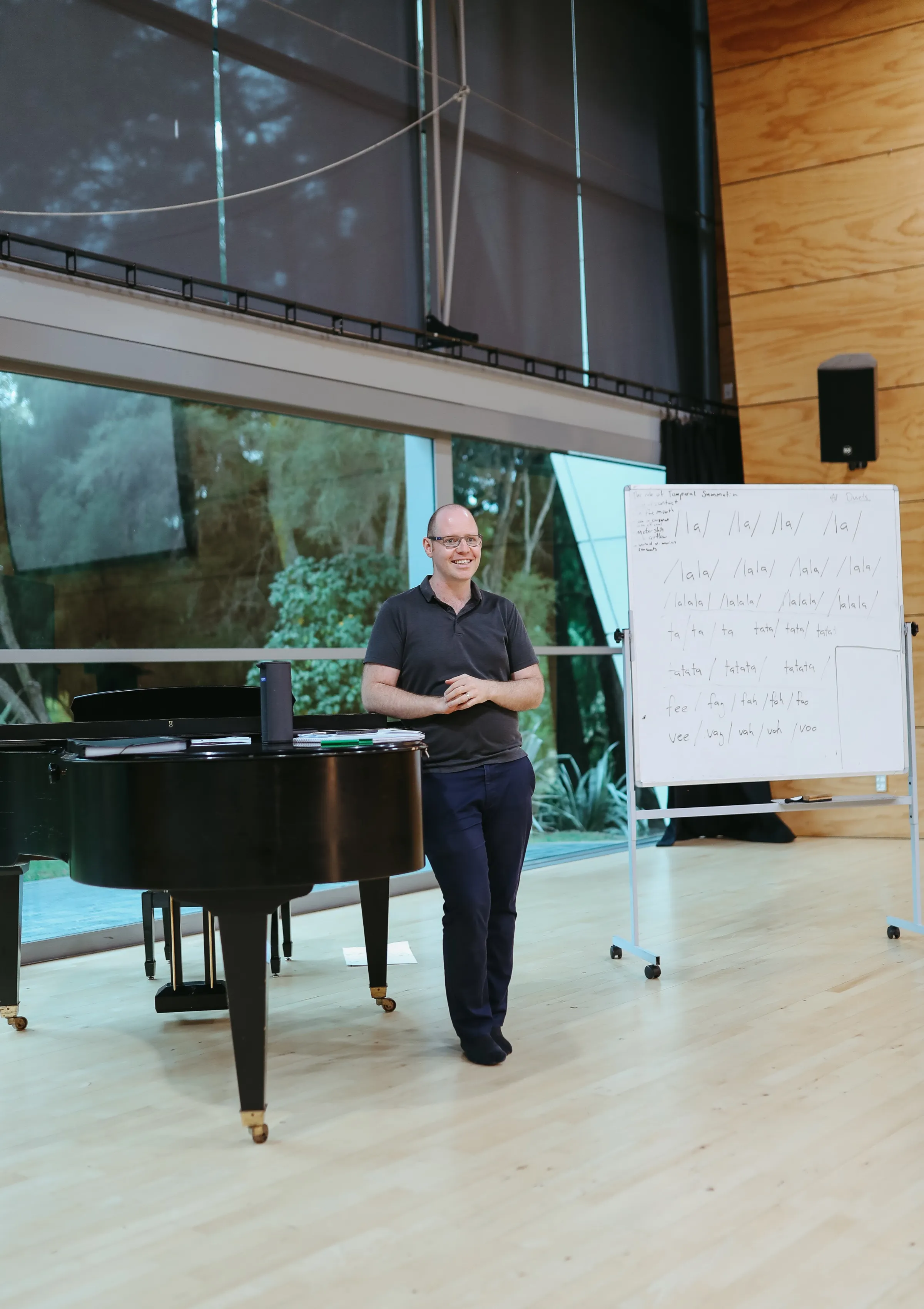 Scot Hall smiling beside a piano and vocal coaching whiteboard
