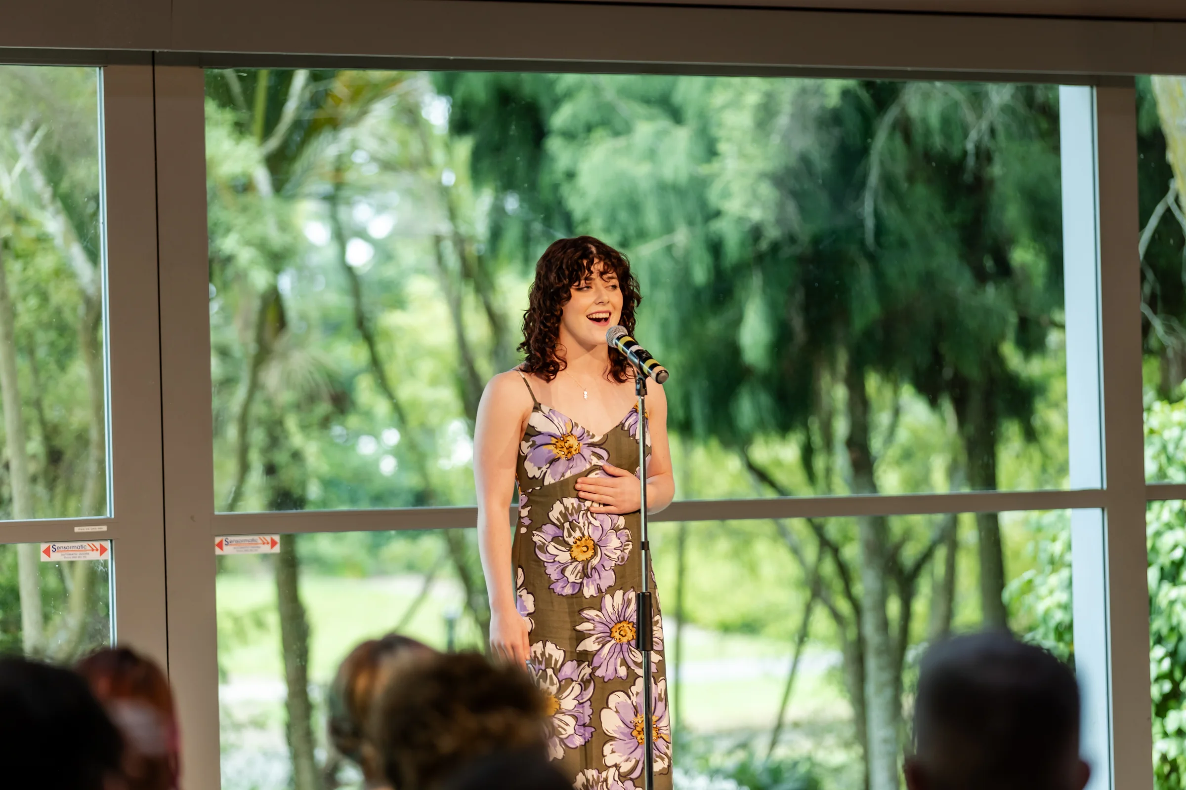 A musical theatre singer performing for an audience in front of bright studio windows