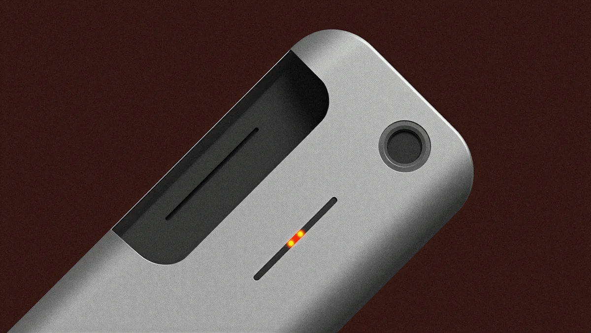 Close-up of a sleek gray electronic device with a slot, two orange indicator lights, and a round button.