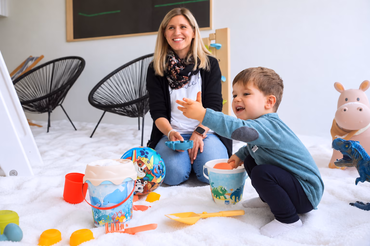 Kind spielt mit Eimern und Schaufeln im bisherigen Kinderluft-Salzraum, eine Begleitperson sitzt daneben