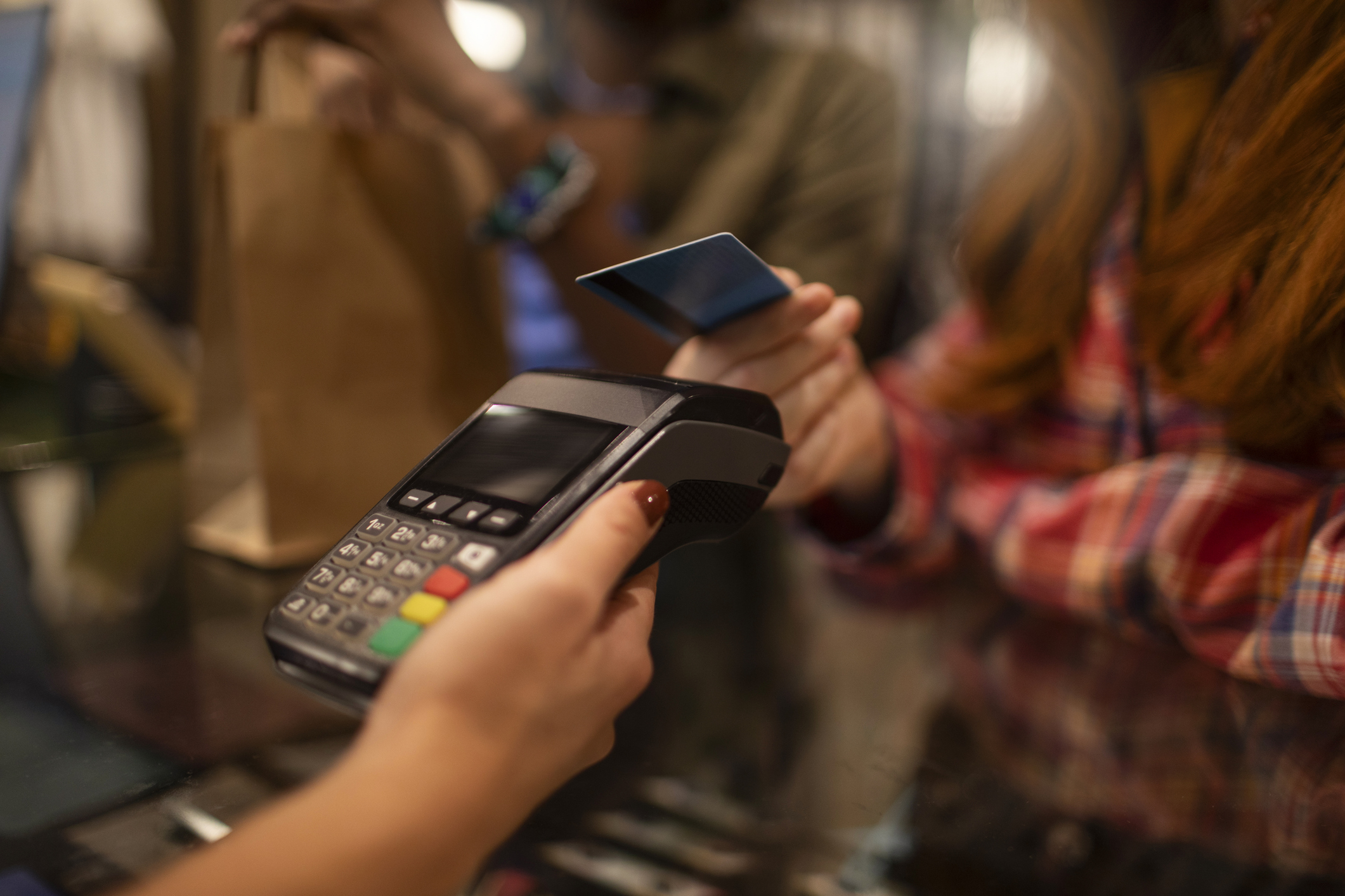 Person holding a credit card near a payment terminal for a contactless transaction, a hand with painted nails holds the terminal.