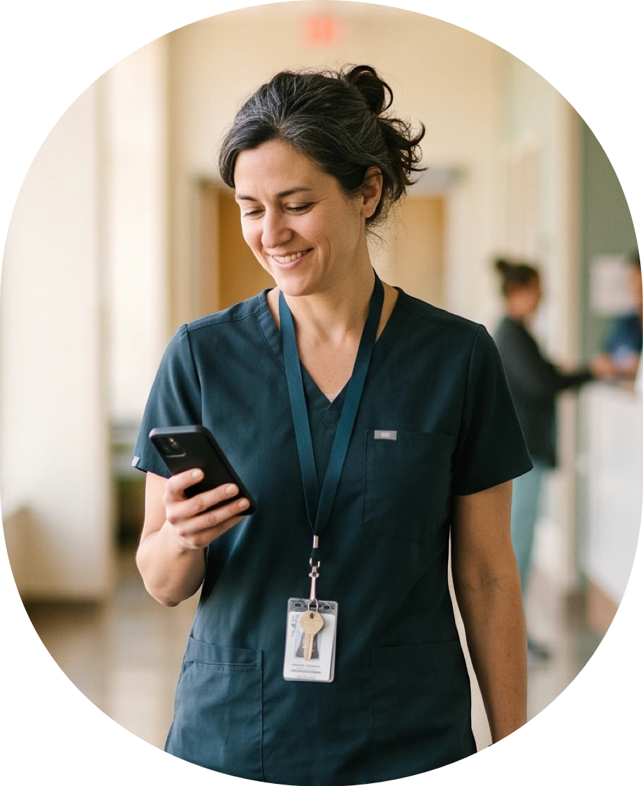 Smiling healthcare worker in scrubs holding a phone in a hallway
