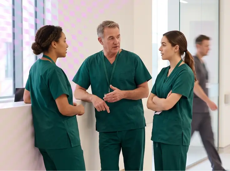 Three healthcare professionals in green scrubs talking in a modern hospital setting