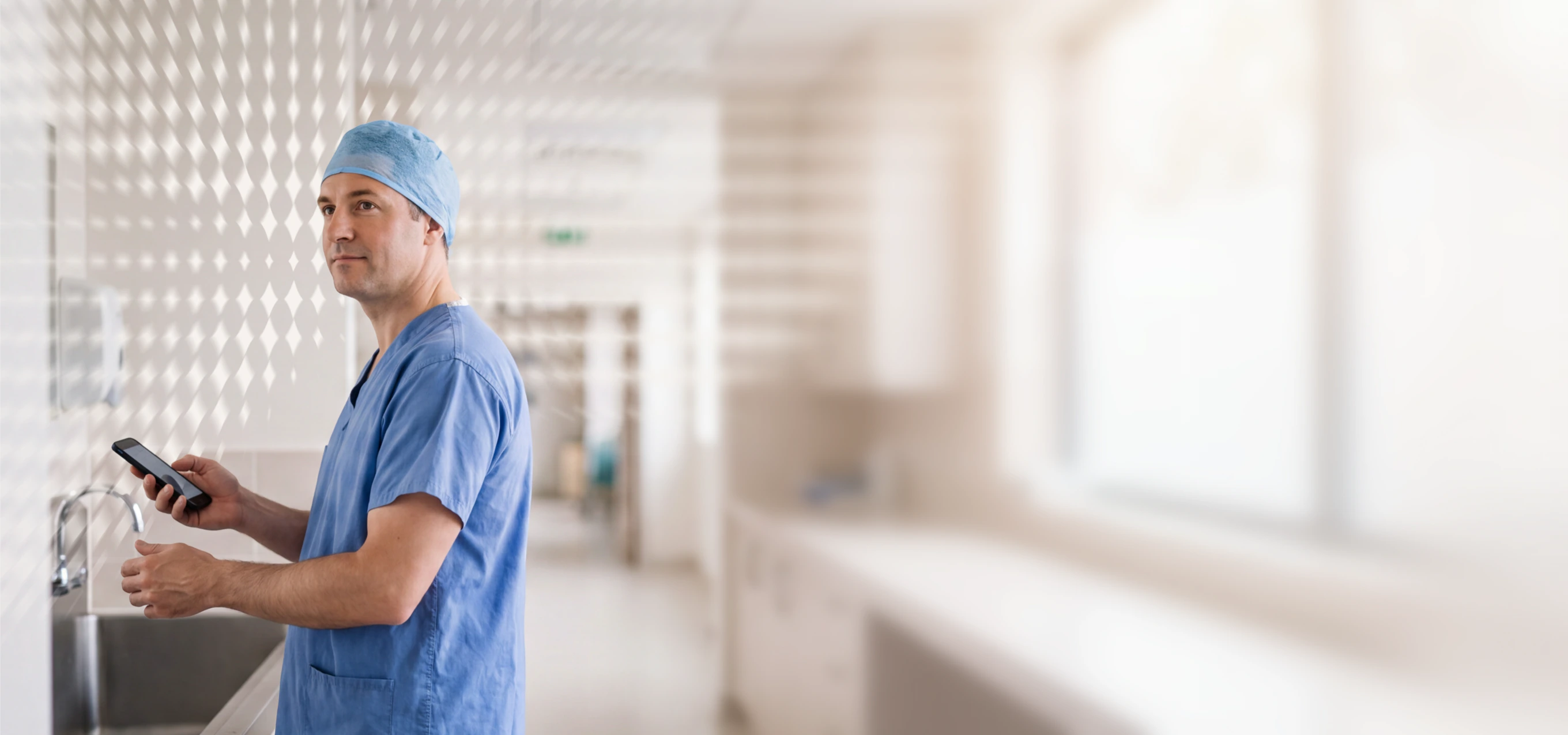 Doctor in scrubs using a smartphone in a hospital corridor