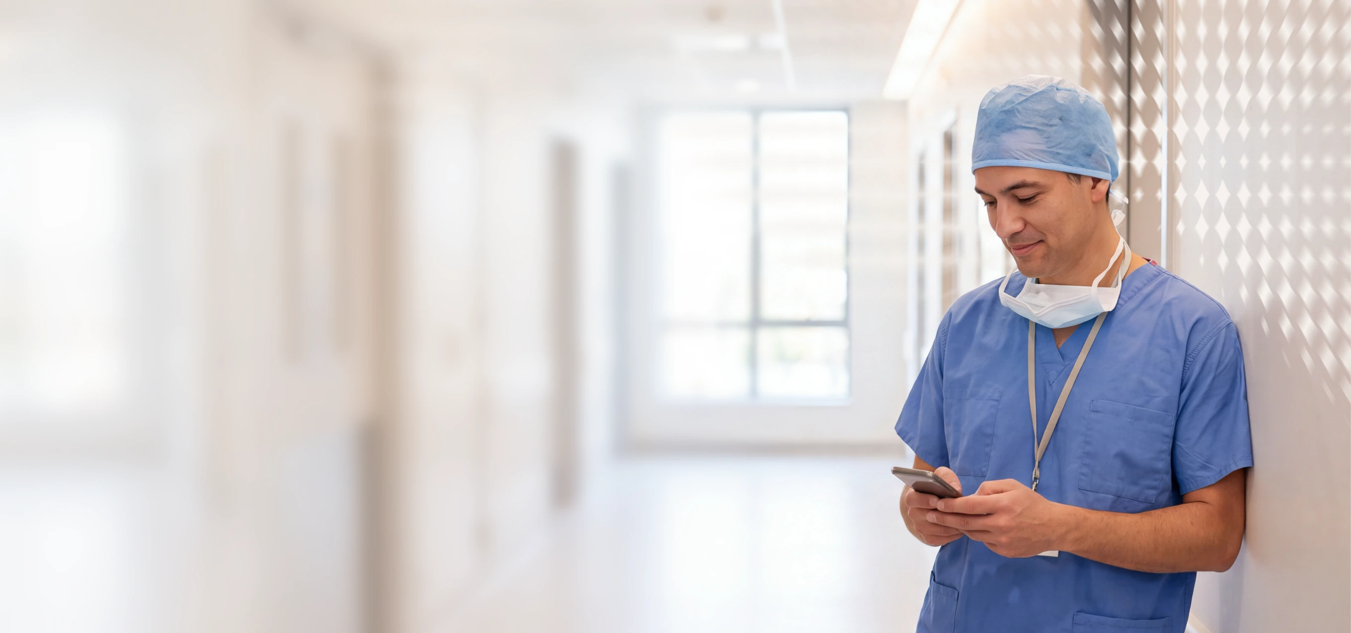 Doctor in scrubs using a phone in a hospital corridor