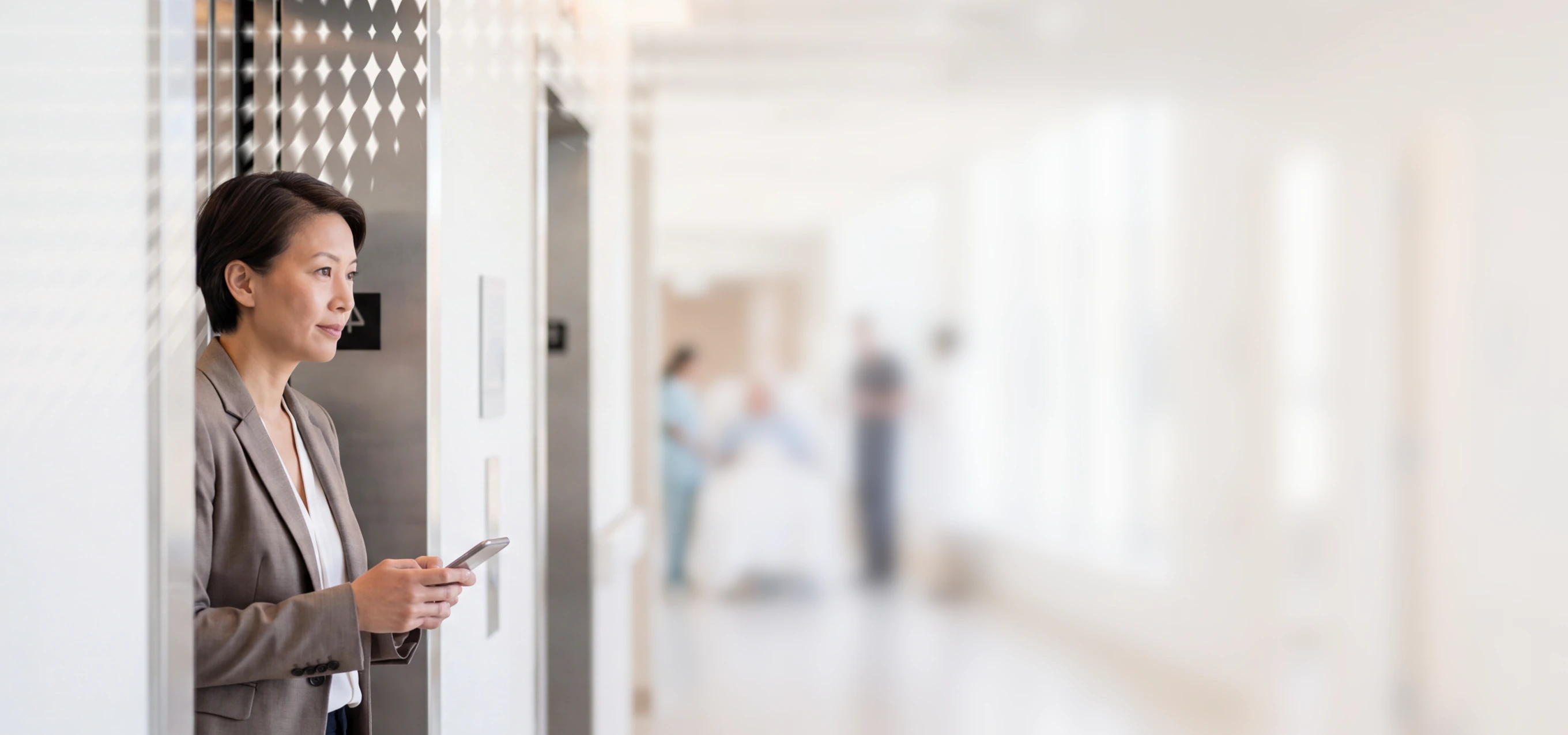 Professional woman in business attire using a phone in an office hallway