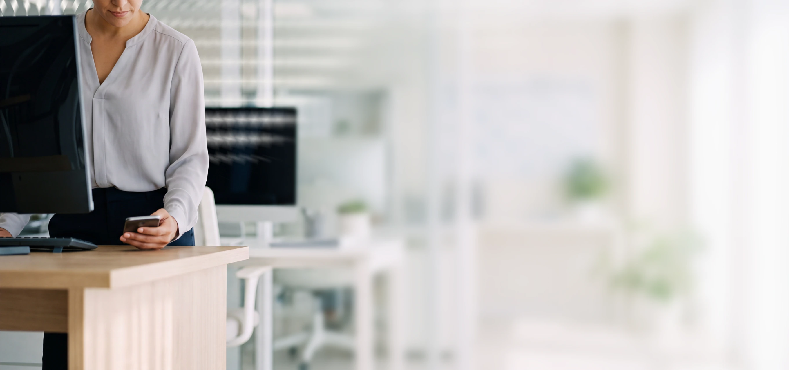 Woman in business attire using a smartphone at a desk in a modern office setting