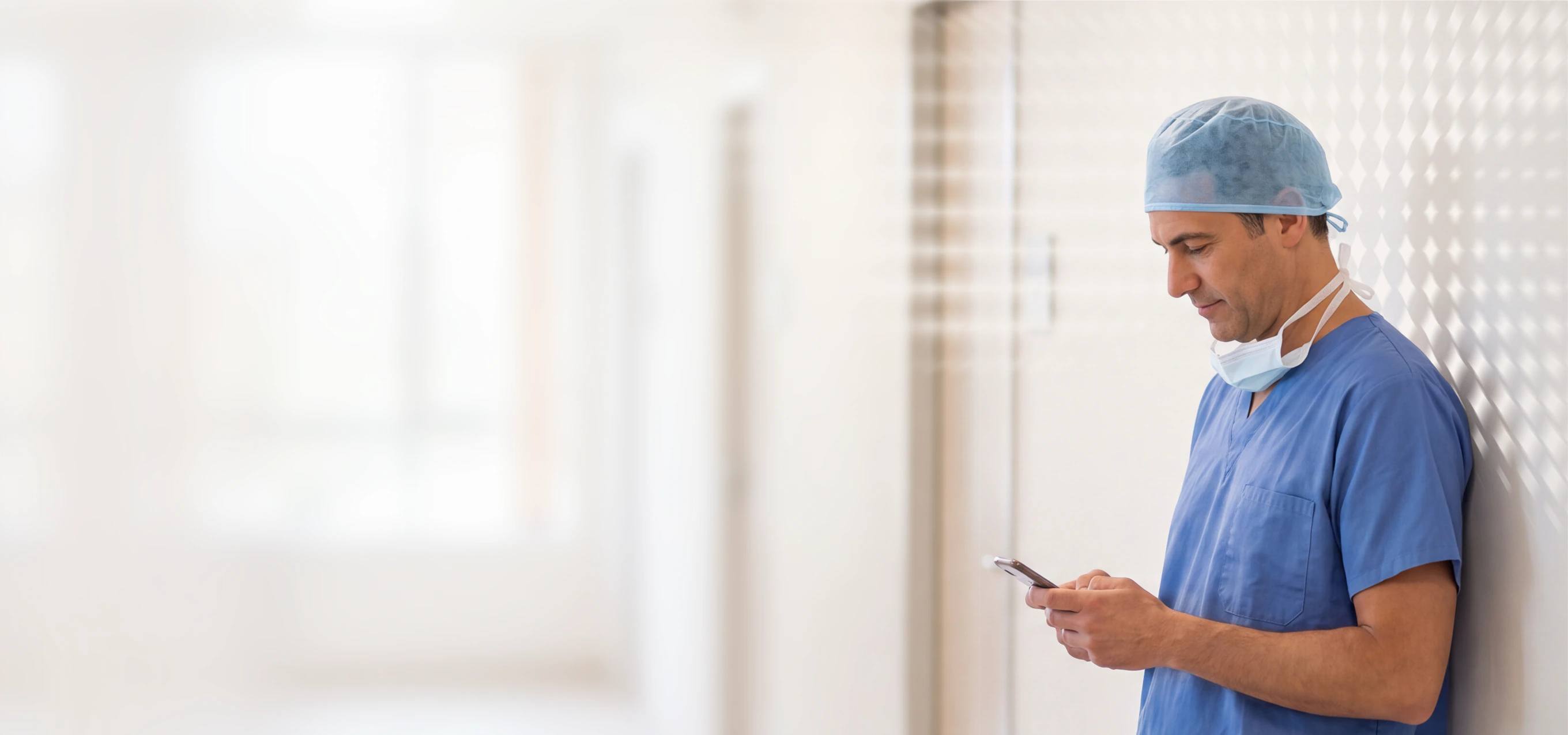 Doctor in scrubs and surgical cap using a phone in a hospital hallway