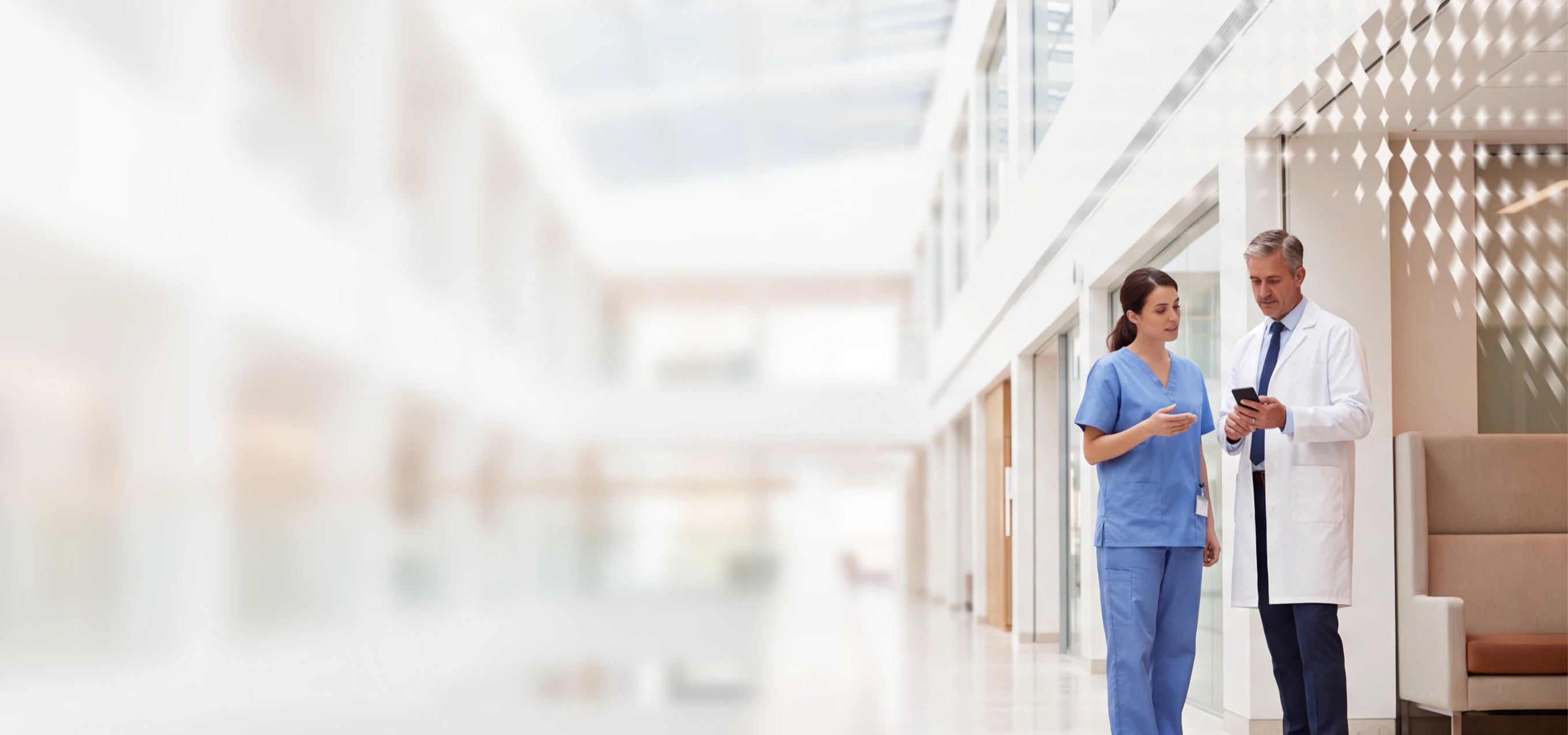 Doctor and nurse in scrubs discussing on phone in modern hospital corridor