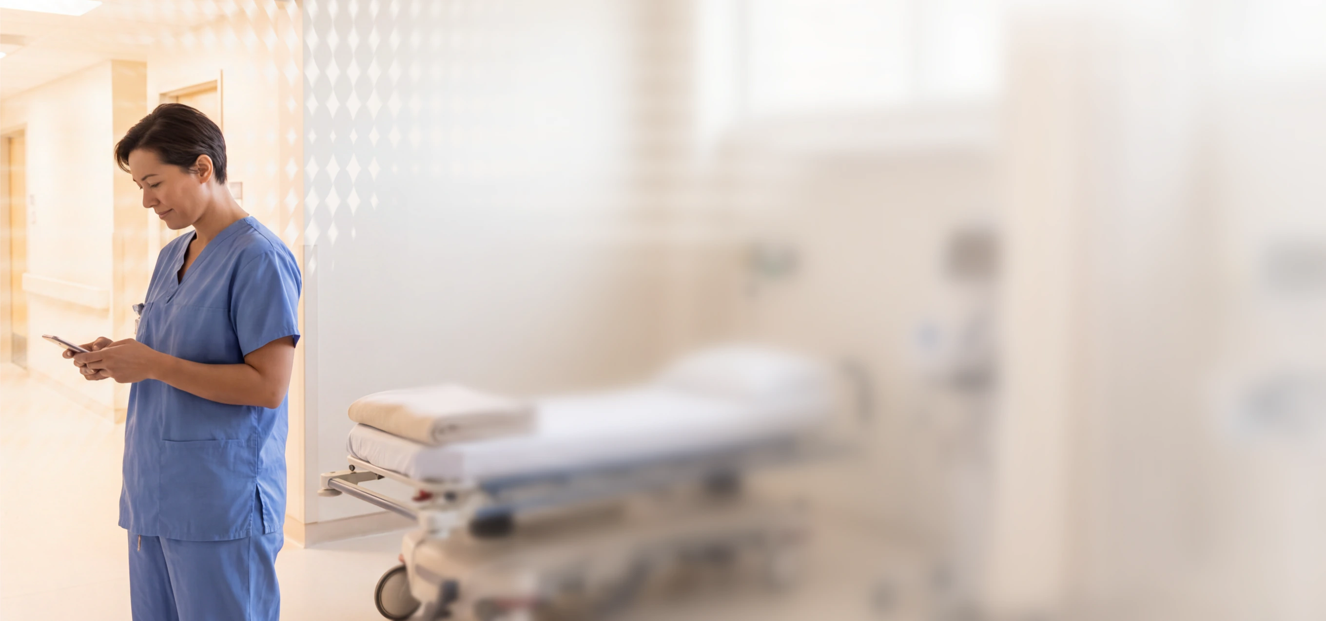 Nurse in scrubs using a phone in a hospital corridor