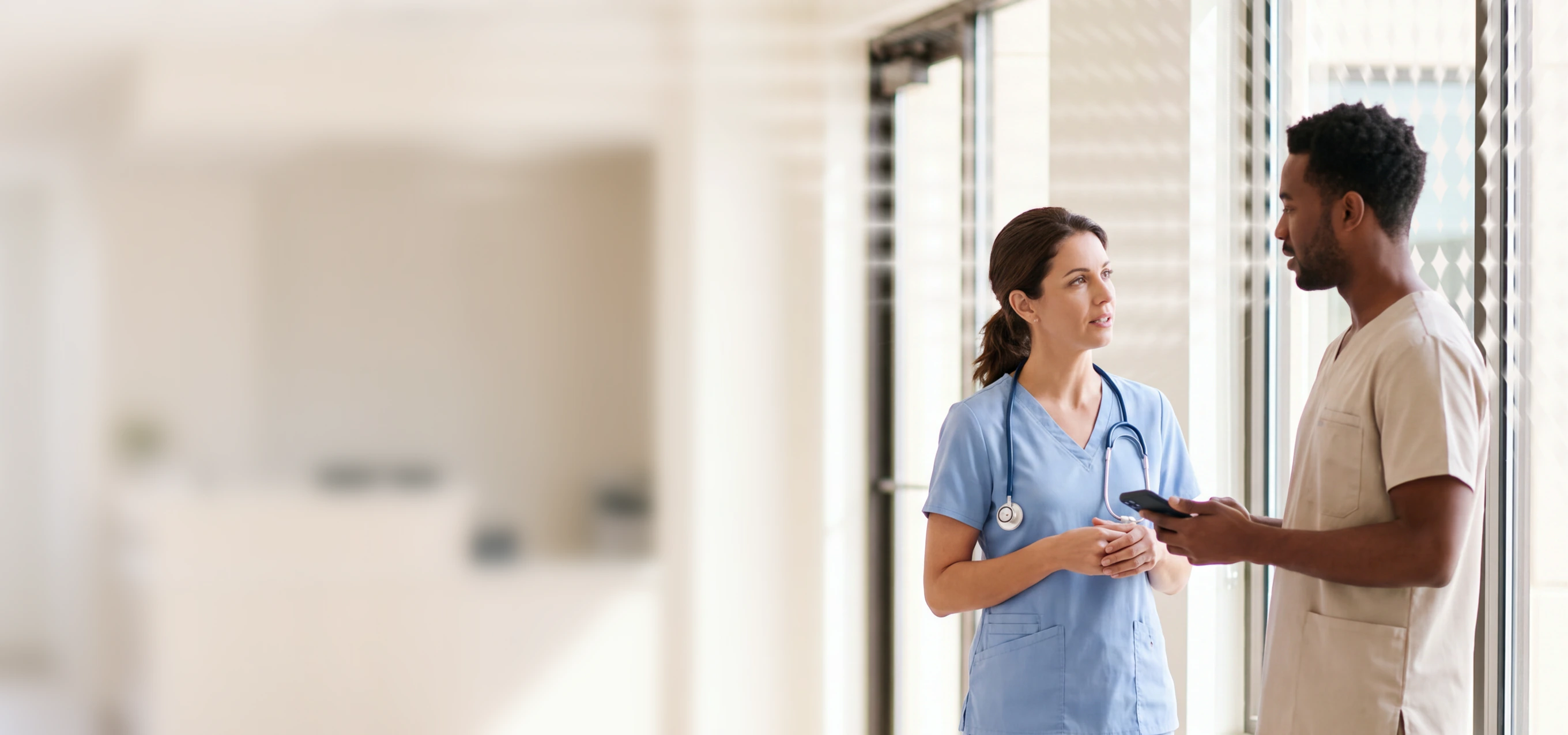 Two healthcare professionals in scrubs talking in a hospital corridor