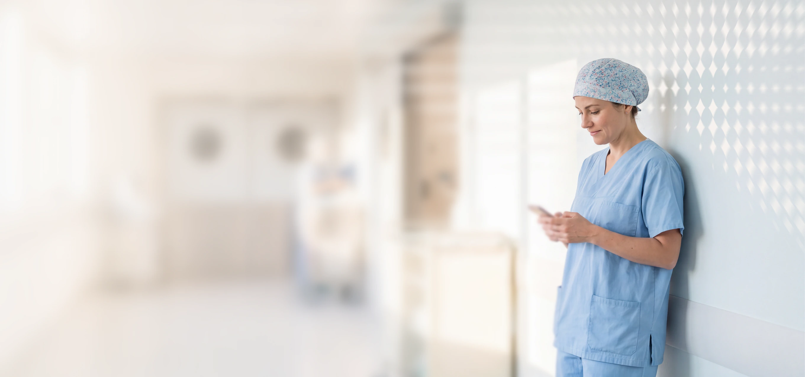 Nurse in scrubs using a phone in a hospital corridor