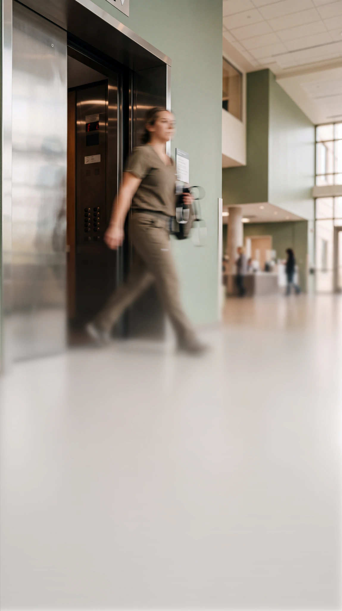 A healthcare worker in scrubs exiting an elevator in a modern building