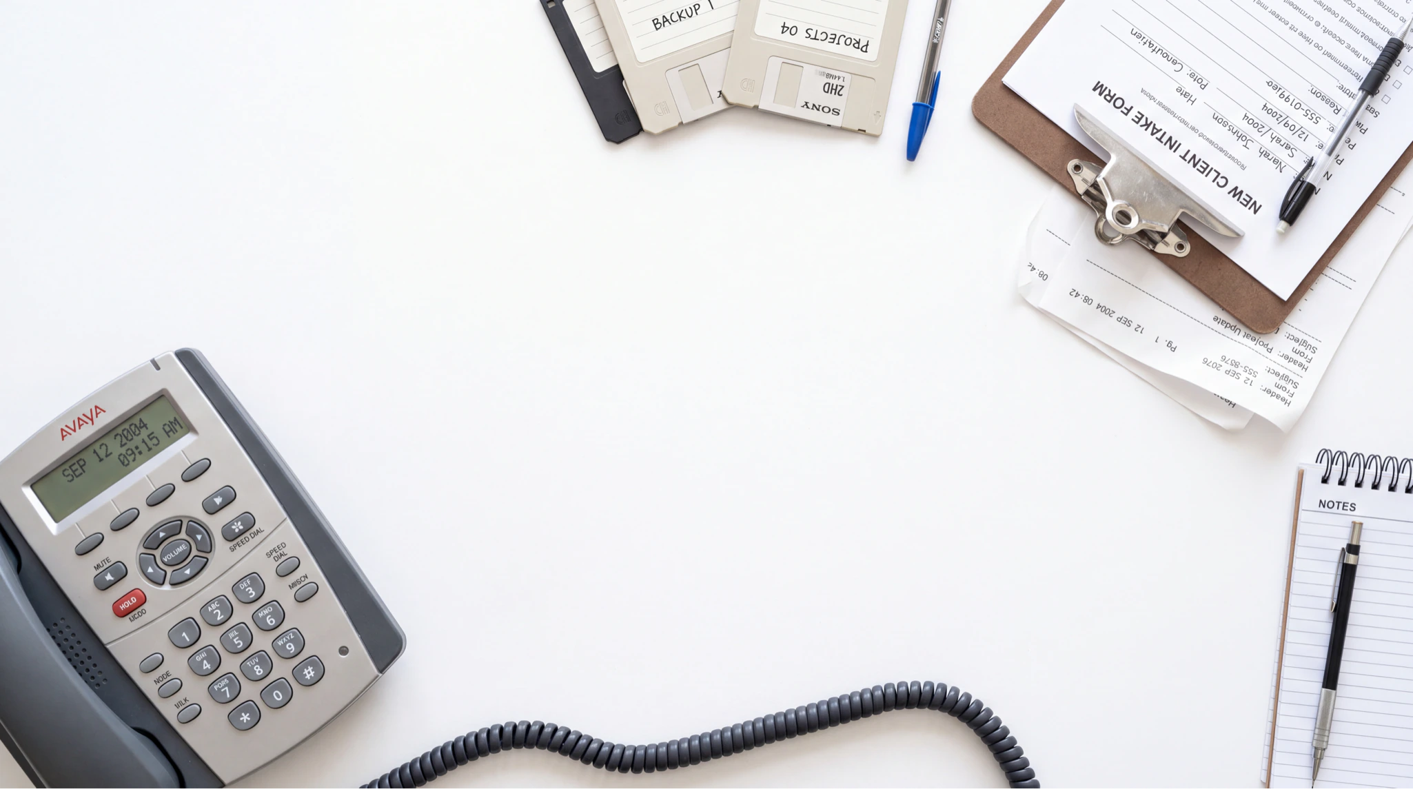 Desk with Avaya phone, floppy disks, clipboard with New Client Intake Form, and notepad with pen