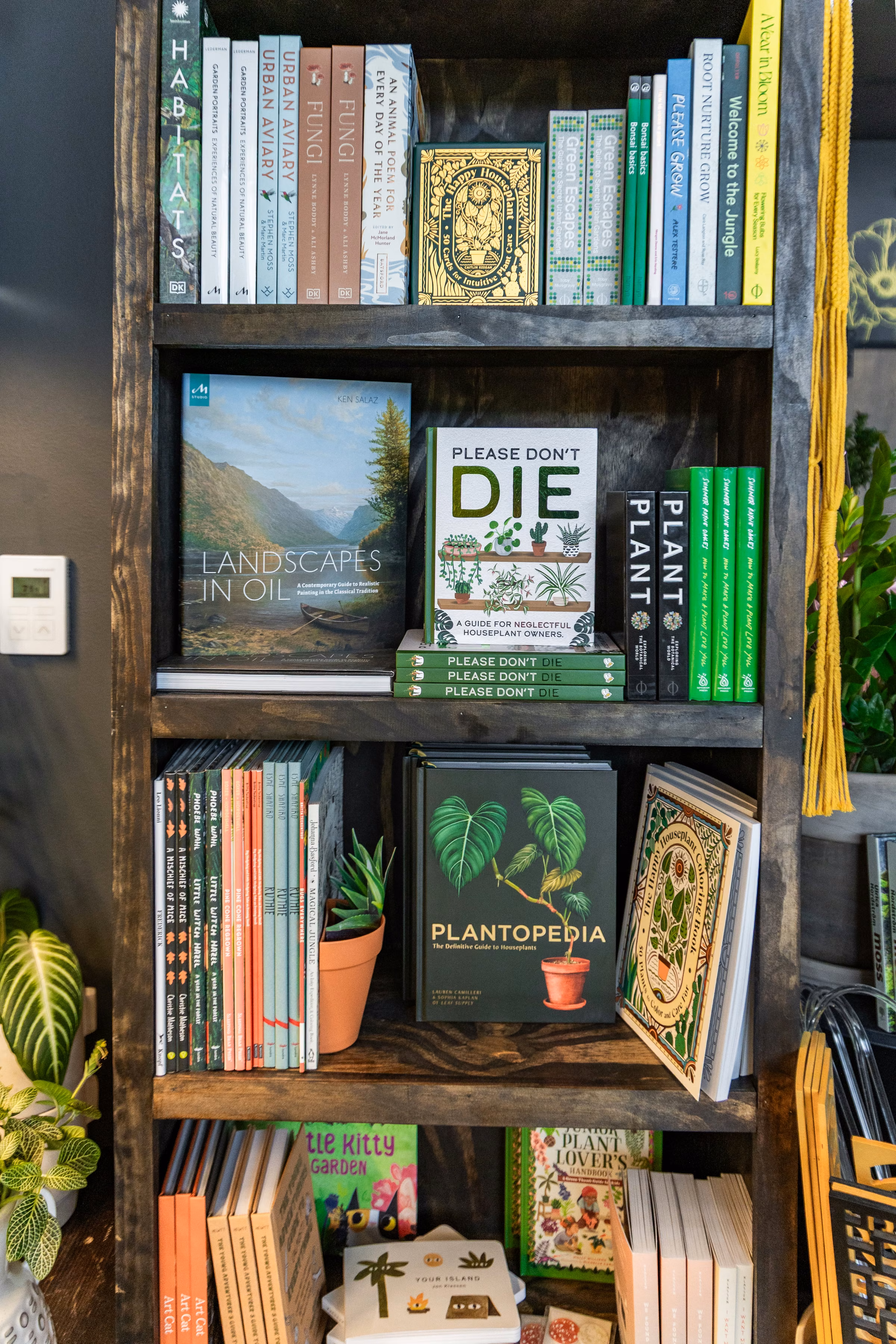 Dark wooden bookcase filled with houseplant and gardening books beside potted greenery