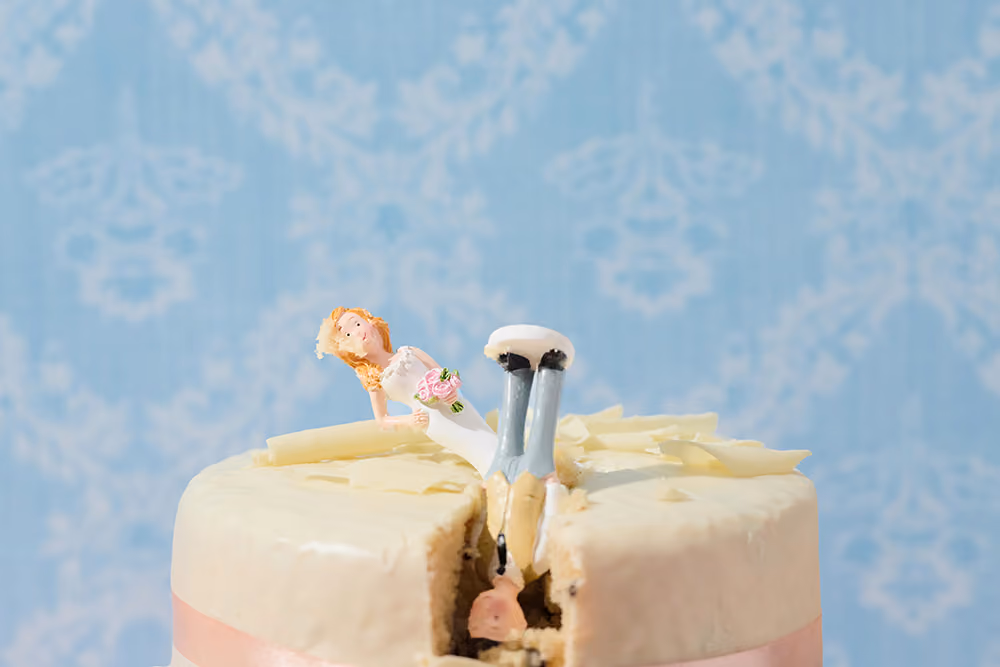 Braut und Bräutigam Hochzeitskuchendekoration, wobei die Brautfigur auf dem Rücken des Bräutigams liegt, beide stecken in einem Kuchen mit hellen Zuckerguß.