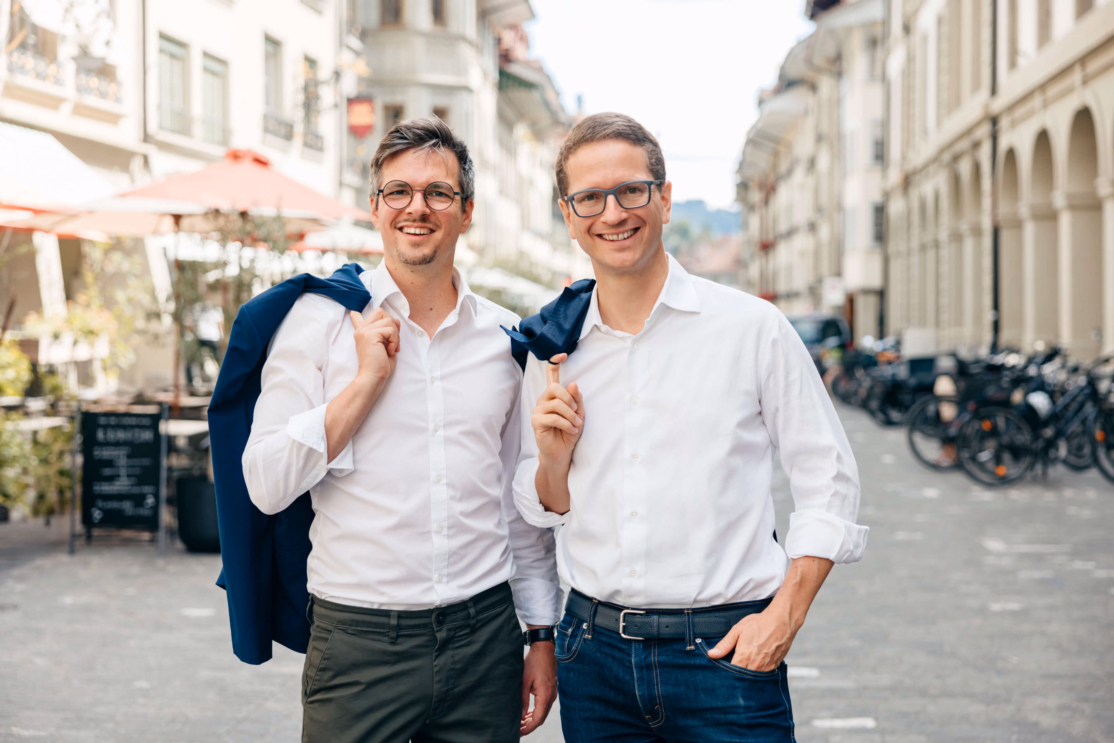 Patrice Choffat und Gabriel Diezi mit weissen Hemden und Jacken über der Schulter auf einer belebten Stadtstrasse.