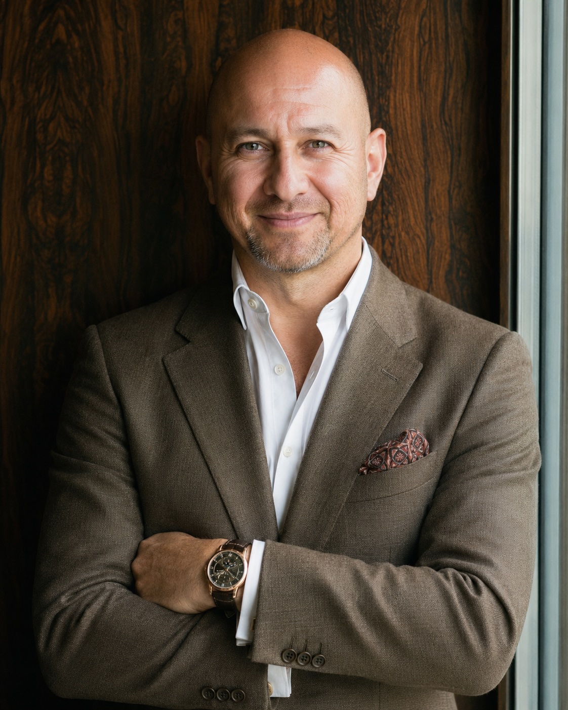 Marvin V. Acuna in a brown blazer with arms crossed against a dark wooden background