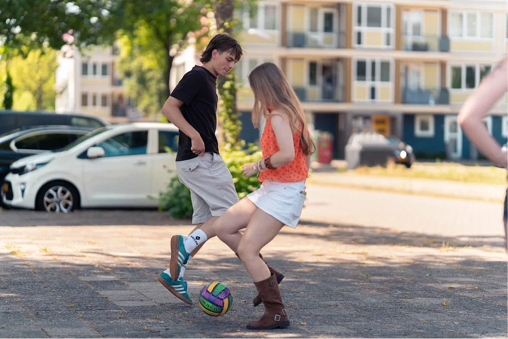 Twee jongeren voetballen samen op straat in een woonwijk in Leeuwarden.