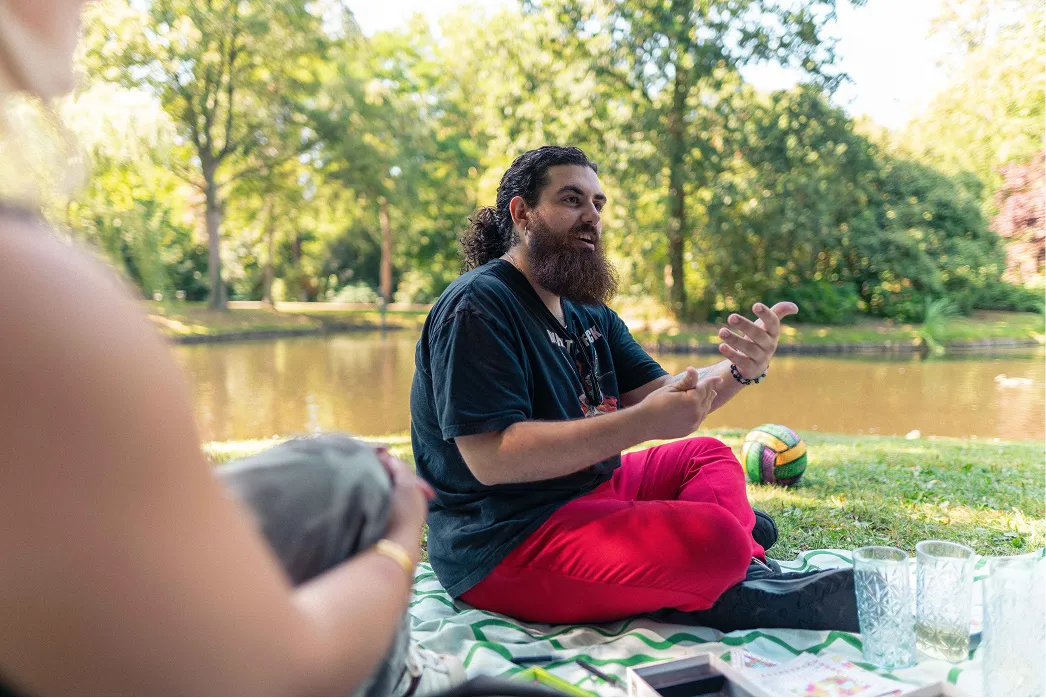 Een jongere vertelt enthousiast zijn verhaal aan anderen tijdens een bijeenkomst in het park.
