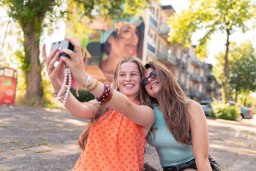 Twee jonge vrouwen maken een selfie op een pleintje in een woonwijk in Leeuwarden.