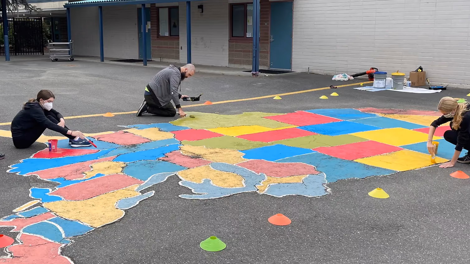 Volunteers painting a map of the United States on school pavement.