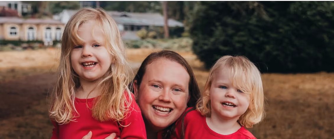 A mother and her two daughters smiling outdoors.