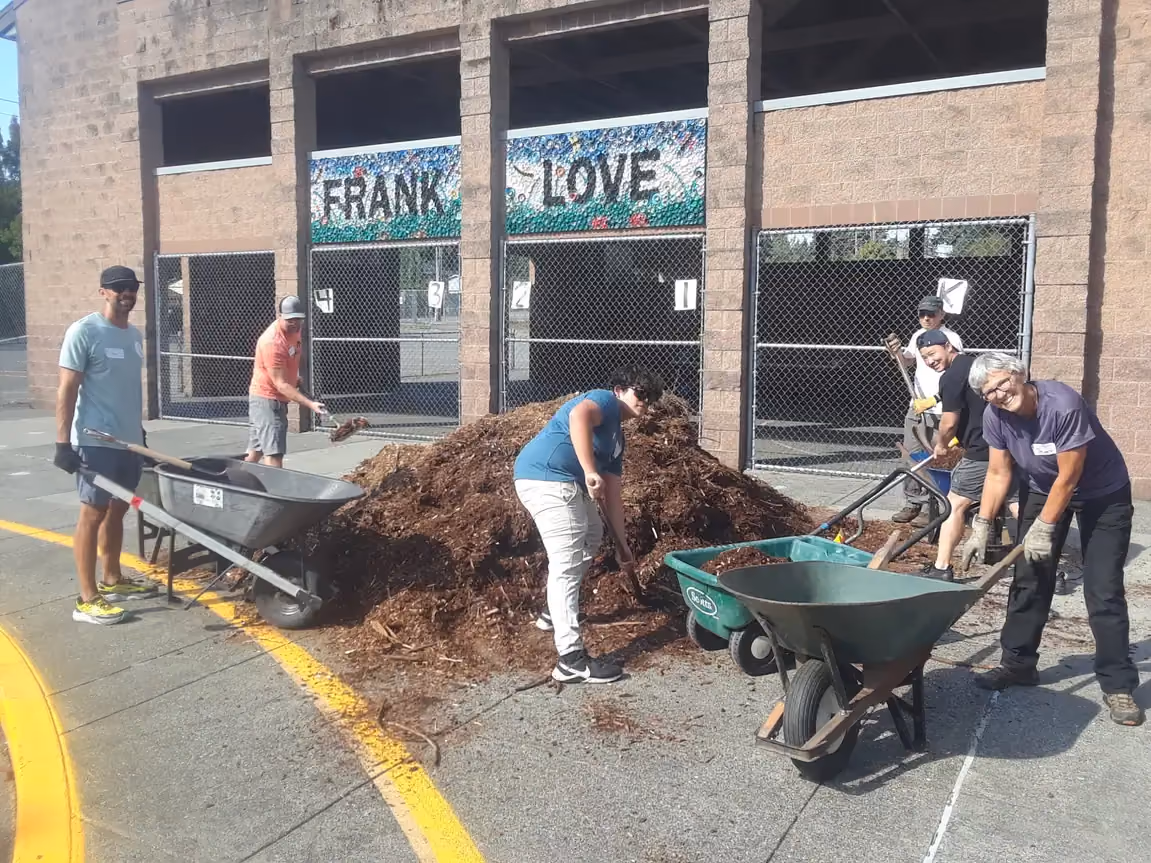 Volunteers moving wood chips outside a building for Community Serve Day.